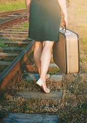 Young woman walking along the rails with a suitcase in her hand, toned.	