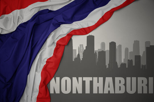 abstract silhouette of the city with text Nonthaburi near waving national flag of thailand on a gray background.3D illustration
