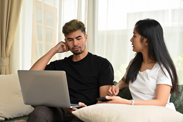 Young Asian couple sitting on sofa together while a man looking on laptop, Domestic life and Domestic home concept.