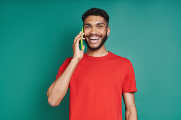 Happy African man talking on mobile phone and smiling while standing against green background