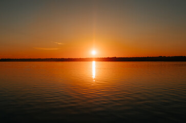 Beautiful colorful orange sunset on lake. Bright sun and reflection on water, natural landscape