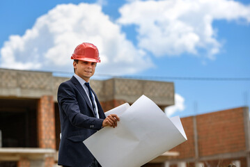 Engineer architect is holding a paper plan of a building at the construction site..