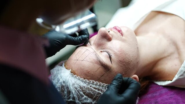 Permanent makeup cosmetologist master takes measurements for the new shape of the eyebrows of model. Microblading preparation