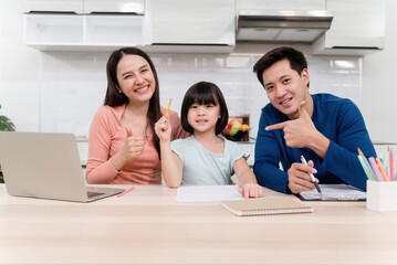 Fototapeta premium Beautiful woman And handsome men are teaching cute Asian girls to draw and write on white paper On the table at home Everyone is happy It's a new normal life for the family.