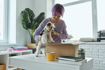 Beautiful young woman and little cute dog looking inside a box