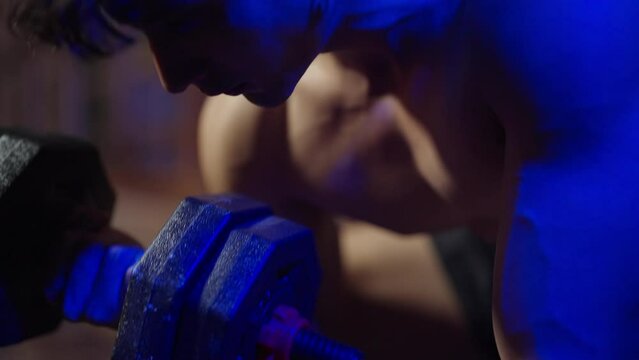 4K Asian sportsman do sport workout weight training exercise in abandoned building. Shirtless man bodybuilder athlete practicing muscular strength bodybuilding lifting heavy dumbbell in dark old gym