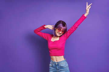 Happy young woman dancing while standing against purple background