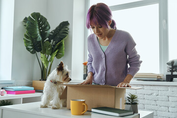 Excited young woman opening box while her cute dog sitting near her on the table