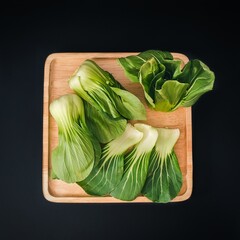 Organic green Baby Bok Choy or Brassica rapa chinensis on wooden plate on black background. Popular Chinese vegetable for Asian cuisine.Healthy vegetarian and vegan eating.