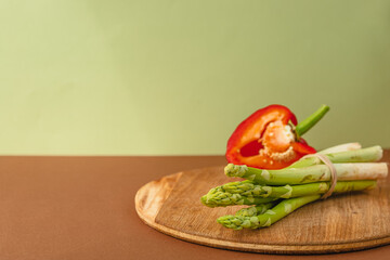 Vegetables lie on a wooden board: asparagus, red bell peppers. brown, light green background. place for text.
