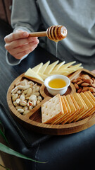 Wooden round menagerie in women's hands. Kitchen plate for snacks, table setting, natural style. Menazhnitsa with snacks, biscuits, cheese, nuts. High quality photo