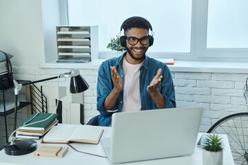 Cheerful young African man having web conference and gesturing while working in office