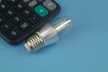 Led light bulb and calculator on blue background with space for text. Energy efficiency of led light lamp concept.
