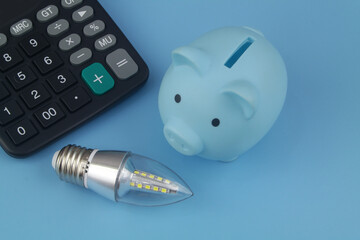 Led light bulb and calculator with piggy bank on blue background. 