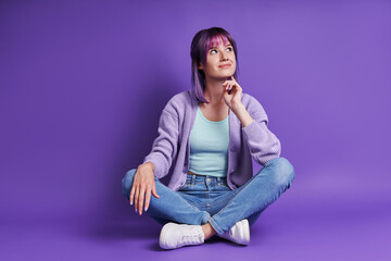 Thoughtful young woman holding hand on chin while sitting against purple background