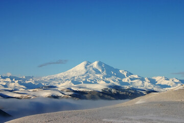 Fototapeta na wymiar Elbrus is a high mountain. Dormant volcano. Mountain covered with snow, blue sky. Caucasus mountains. Fog and slopes