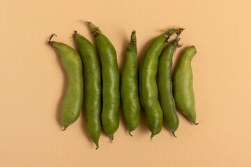 Broad beans in the pod on a beige background. Top view.
