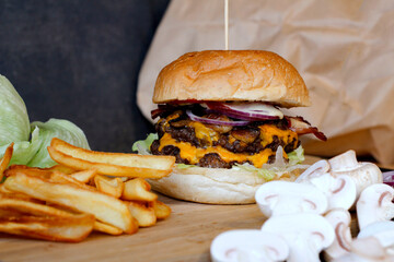 Burger w artystycznej kompozycji z frytkami i batatami oraz cebulą pieczarkami. Burgerownia - zdjęcie świeżego, apetycznego burgera