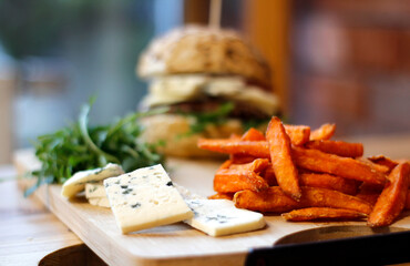 Burger w artystycznej kompozycji z frytkami i batatami oraz cebulą pieczarkami. Burgerownia - zdjęcie świeżego, apetycznego burgera