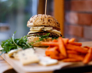 Burger w artystycznej kompozycji z frytkami i batatami oraz cebulą pieczarkami. Burgerownia - zdjęcie świeżego, apetycznego burgera