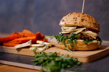Burger w artystycznej kompozycji z frytkami i batatami oraz cebulą pieczarkami. Burgerownia - zdjęcie świeżego, apetycznego burgera