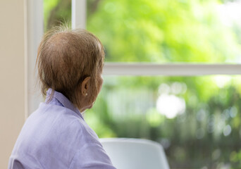 Senior Woman With Hair Loss After Chemotherapy From Breast Cancer Sitting Alone at Home looking Out...