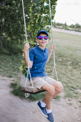 a boy in sunglasses rides on a swing in the park in summer