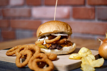 Burger w artystycznej kompozycji z frytkami i batatami oraz cebulą pieczarkami. Burgerownia - zdjęcie świeżego, apetycznego burgera