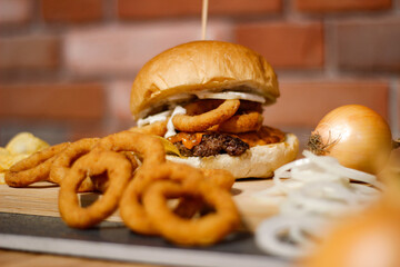 Burger w artystycznej kompozycji z frytkami i batatami oraz cebulą pieczarkami. Burgerownia - zdjęcie świeżego, apetycznego burgera