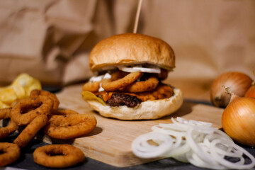 Burger w artystycznej kompozycji z frytkami i batatami oraz cebulą pieczarkami. Burgerownia - zdjęcie świeżego, apetycznego burgera
