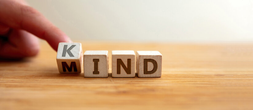 Kind mind concept. Finger flips letter at wooden cube changing the word mind to kind. Banner