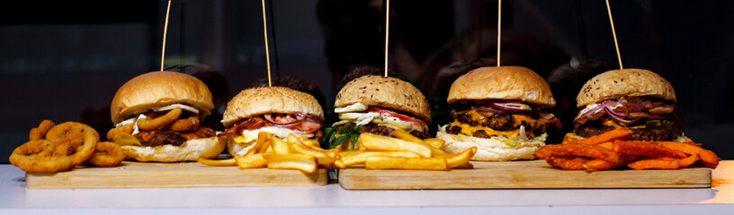 Burger w artystycznej kompozycji z frytkami i batatami oraz cebulą pieczarkami. Burgerownia - zdjęcie świeżego, apetycznego burgera - obrazy, fototapety, plakaty