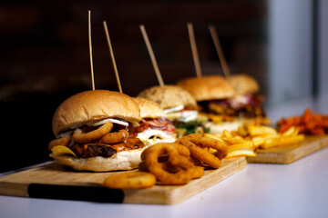 Burger w artystycznej kompozycji z frytkami i batatami oraz cebulą pieczarkami. Burgerownia - zdjęcie świeżego, apetycznego burgera