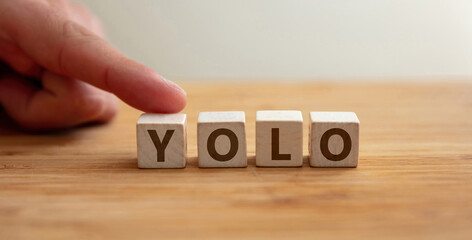 Yolo concept. Word yolo on wooden cube with finger to shows letter y. You Only Live Once phrase.