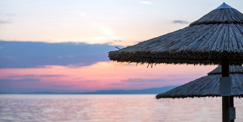 Sunset on the beach. Greece. Straw umbrella, reflection on rippled ocean water.