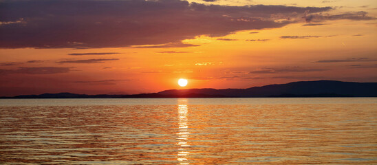 Sunset over Aegean Sea. Greece. Golden reflection on rippled ocean water. Dark land and colorful sky