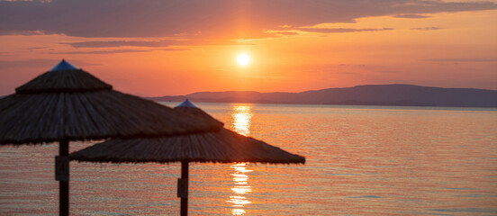 Sunset on the beach. Greece. Straw umbrella silhouette, golden reflection on rippled ocean water.
