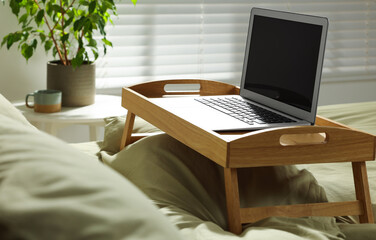 Wooden tray with modern laptop on bed indoors