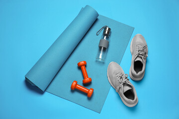 Naklejka premium Exercise mat, dumbbells, shoes and bottle of water on turquoise background, flat lay