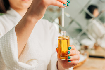 Fototapeta premium Facial Skincare. Happy Korean asian woman applying Facial serum using dropper standing in modern bathroom.