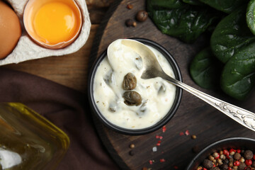 Caper sauce in bowl and ingredients on wooden table, flat lay