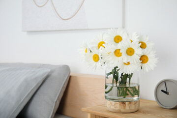 Bouquet of beautiful daisy flowers and clock on wooden table in bedroom, space for text