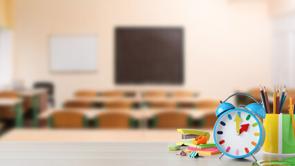 Light blue alarm clock and different stationery on wooden table in classroom, space for text