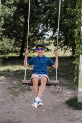 a boy in sunglasses rides on a swing in the park in summer