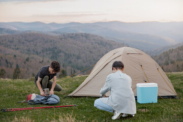 Couple of friends setting camp tent in mountains. Amazing view on landscape. Traveling.