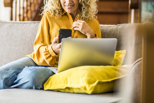 Home leisure activity and technology connection. Woman relaxing on the sofa and use phone and laptop together. Female people with cellular. Communication and social miedia concept
