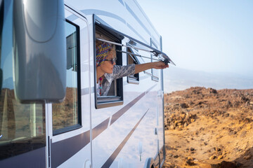 Woman opening caravan window in free parking outdoors admiring the nature outside. Travel and...