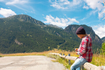 Fototapeta na wymiar Outdoor leisure activity in mountains holiday vacation. Woman sitting on the wood and admiring landscape. Beautiful nature park in background with top valley and sky. Copy space scenic place