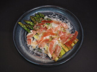 Grilled Asparagus with Ham served in a dish isolated on dark background top view