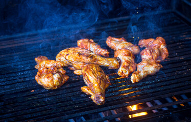 Tasty chicken legs and wings on the grill with fire flames smoke. with cop space